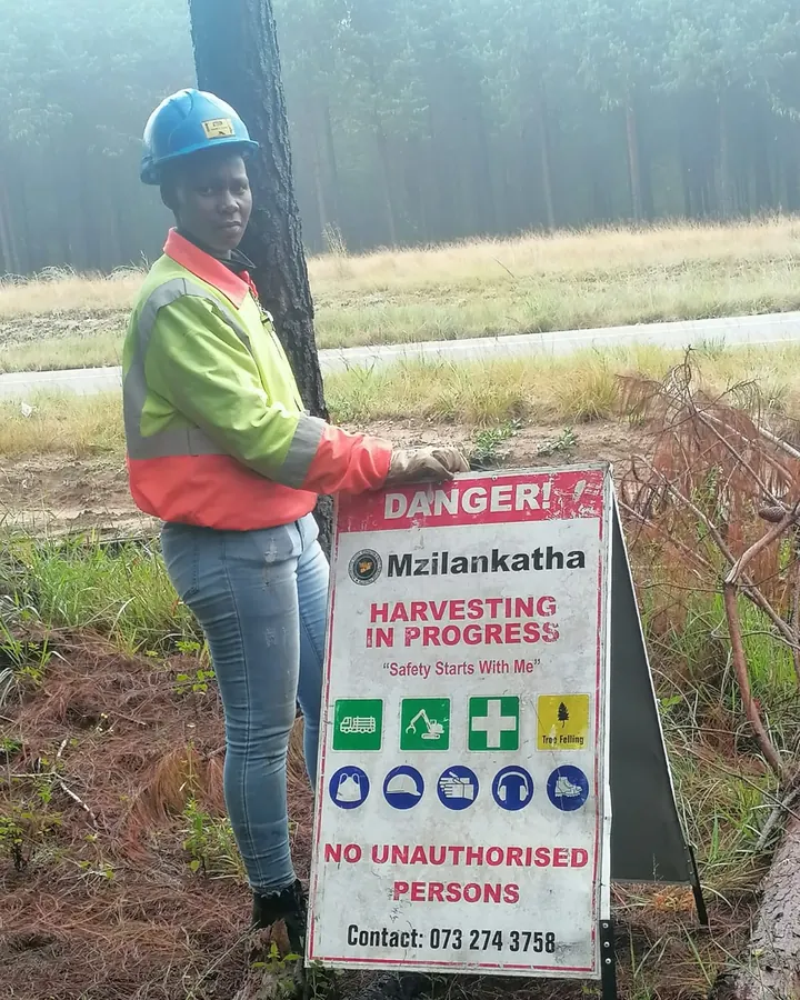 Simphiwe Nakosi, pruning supervisor, in a hard hat and hi-vis jacket beside a danger board that reads Harvesting in progress, No unauthorised persons.