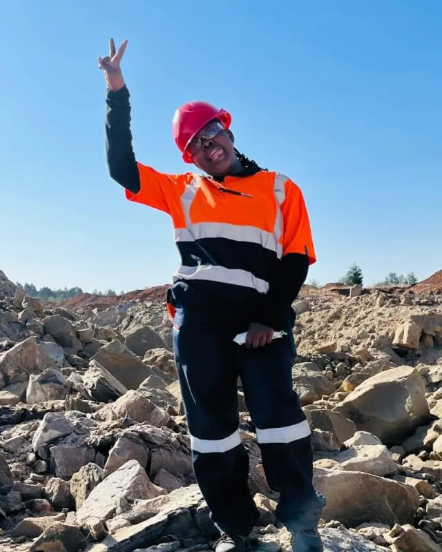 Siphosethu Lukhele in a red hard hat, safety glasses and hi-vis shirt, standing on rocky ground.