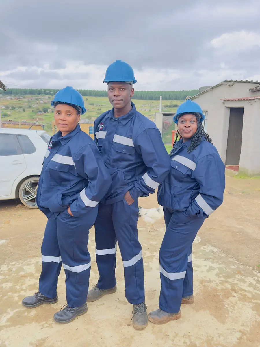 Three members of the spraying team in navy overalls with reflective strips and blue hard hats.